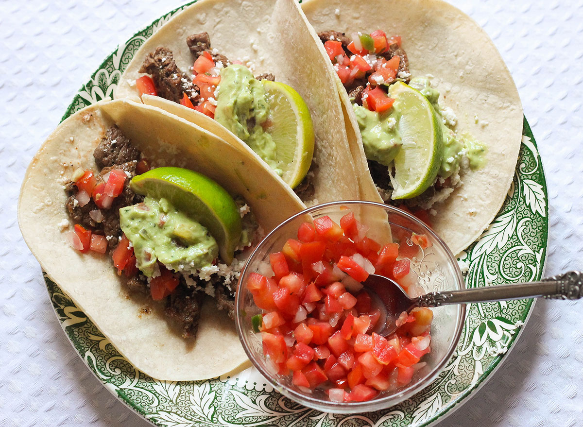 Steak tacos with pico de gallo on a green plate.