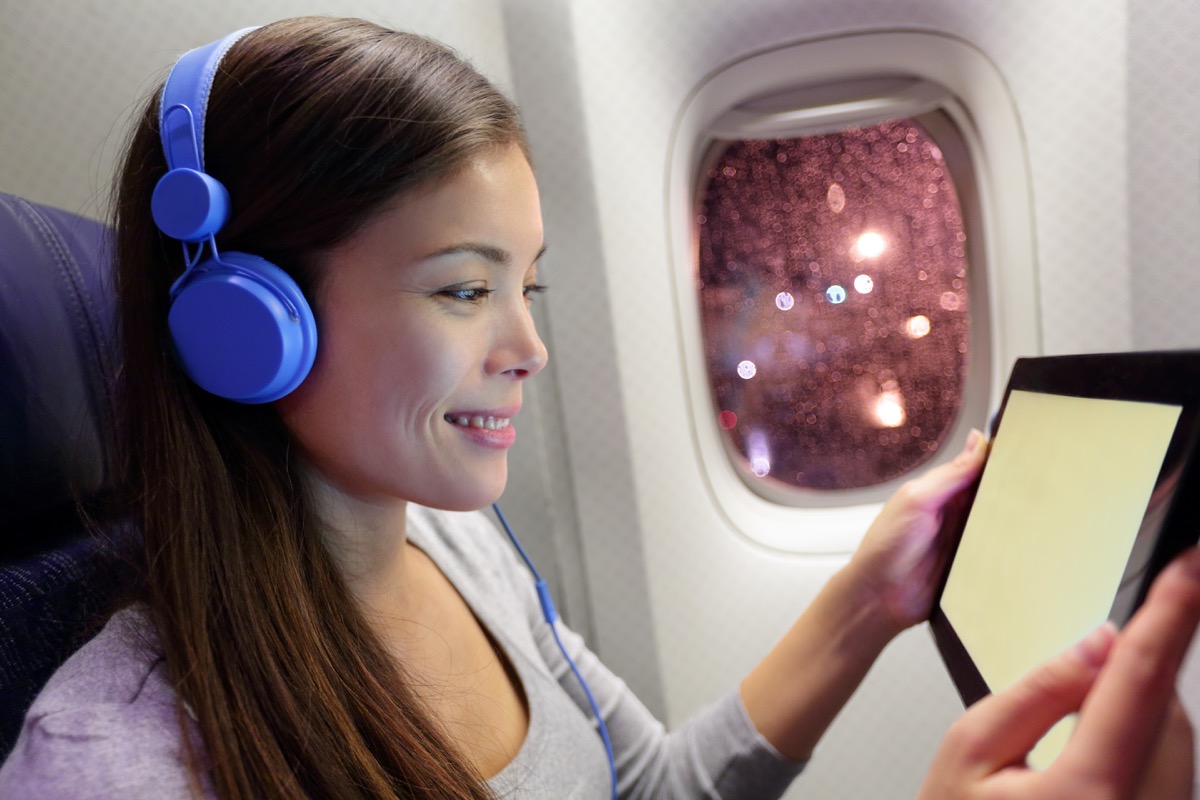 Passenger in airplane using tablet computer. Woman in plane cabin using smart device listening to music on headphones