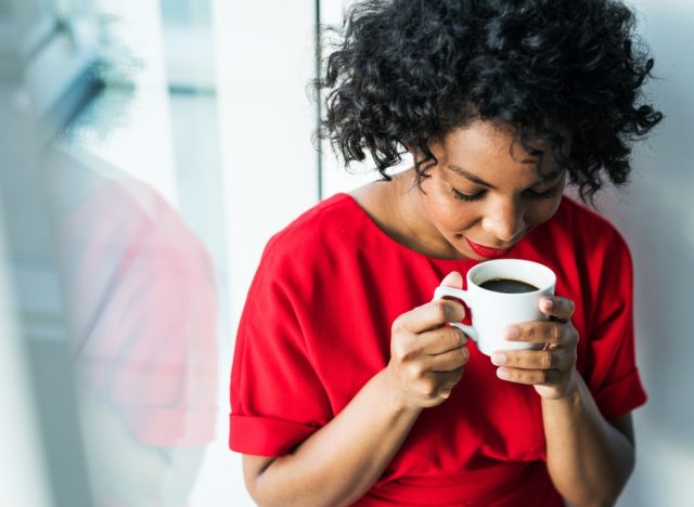 A close-up of a woman standing by the window holding a cup of coffee.