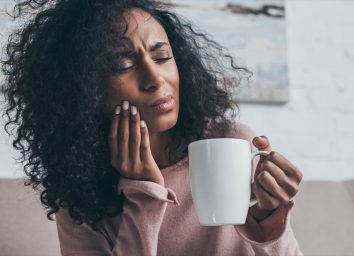 unhappy african american woman suffering from toothache and holding coffee cup