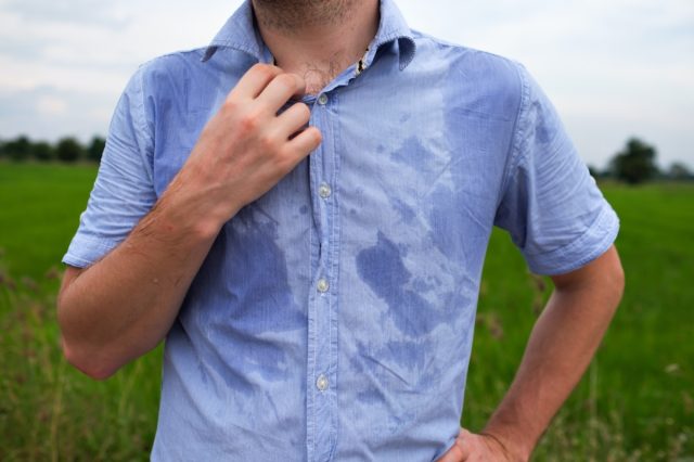 Man with hyperhidrosis sweating very badly under armpit in blue shirt because of hot weather