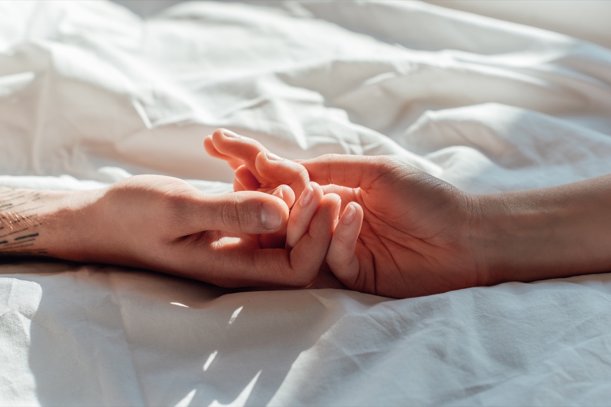 couple in live holding hads while lying in bed together