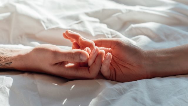 couple in live holding hads while lying in bed together