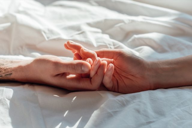 couple in live holding hands while lying in bed together