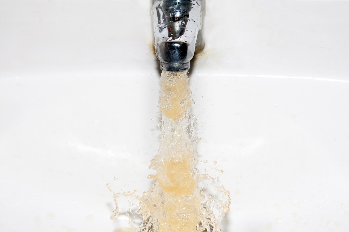 Dirty brown running water falling into a white sink from tap
