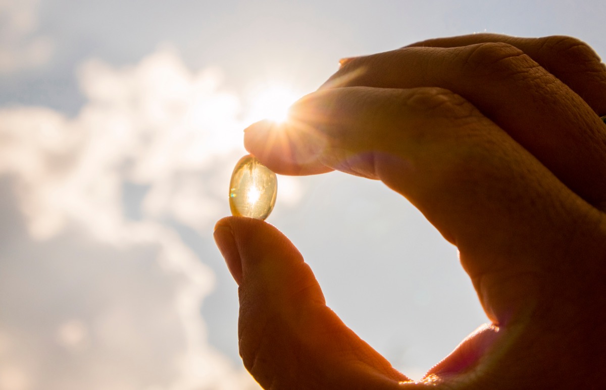 Yellow soft shell D-vitamin capsule against sun and blue sky on sunny day