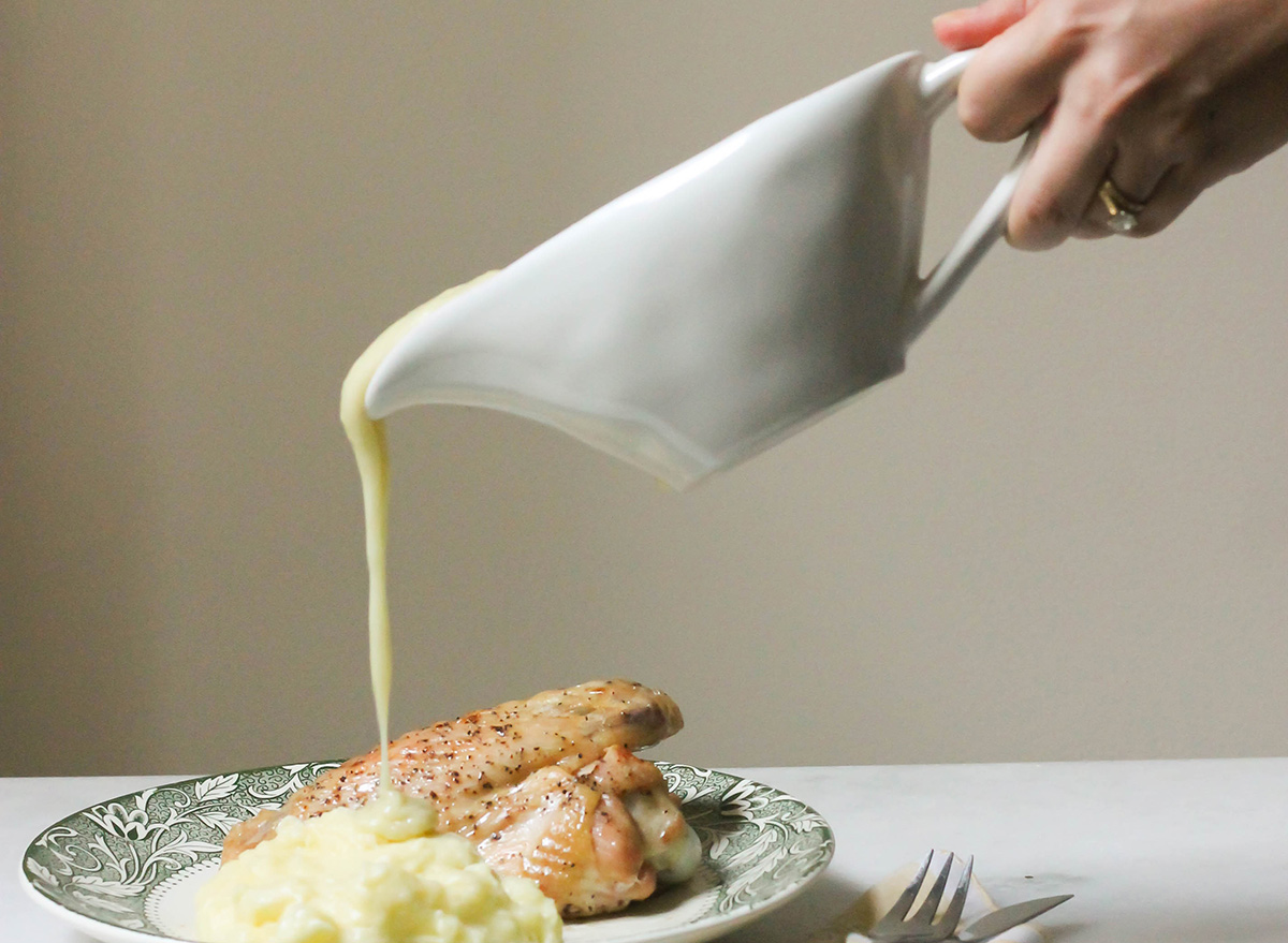 Pouring homemade gravy from a gravy boat onto a plate with mashed potatoes