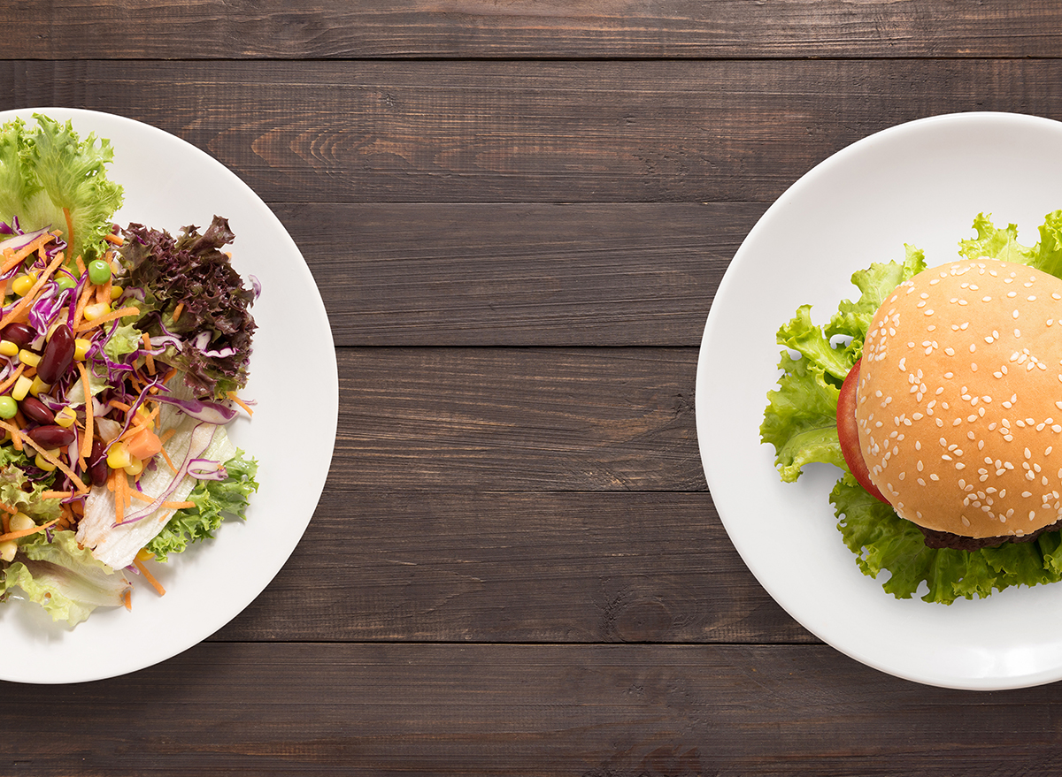 a salad sits next to a burger on a wooden table