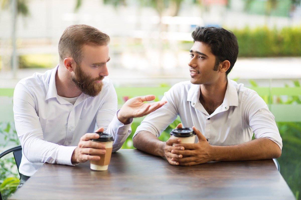 Two male friends drinking coffee and chatting in outdoor cafe.