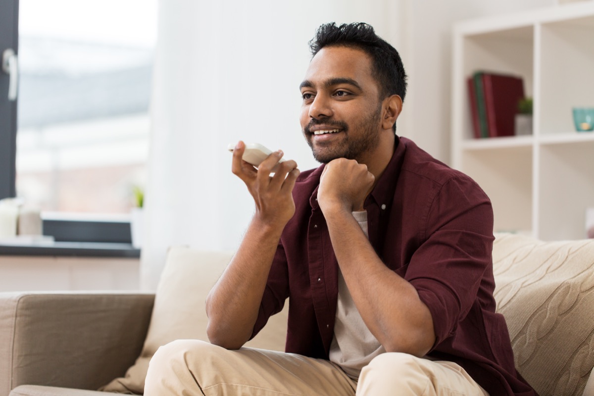 smiling man using voice command recorder on smartphone at home