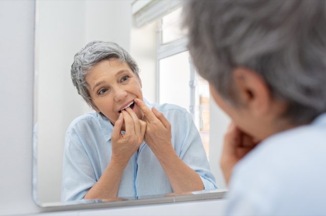 Mature beautiful woman cleaning her teeth with floss in bathroom