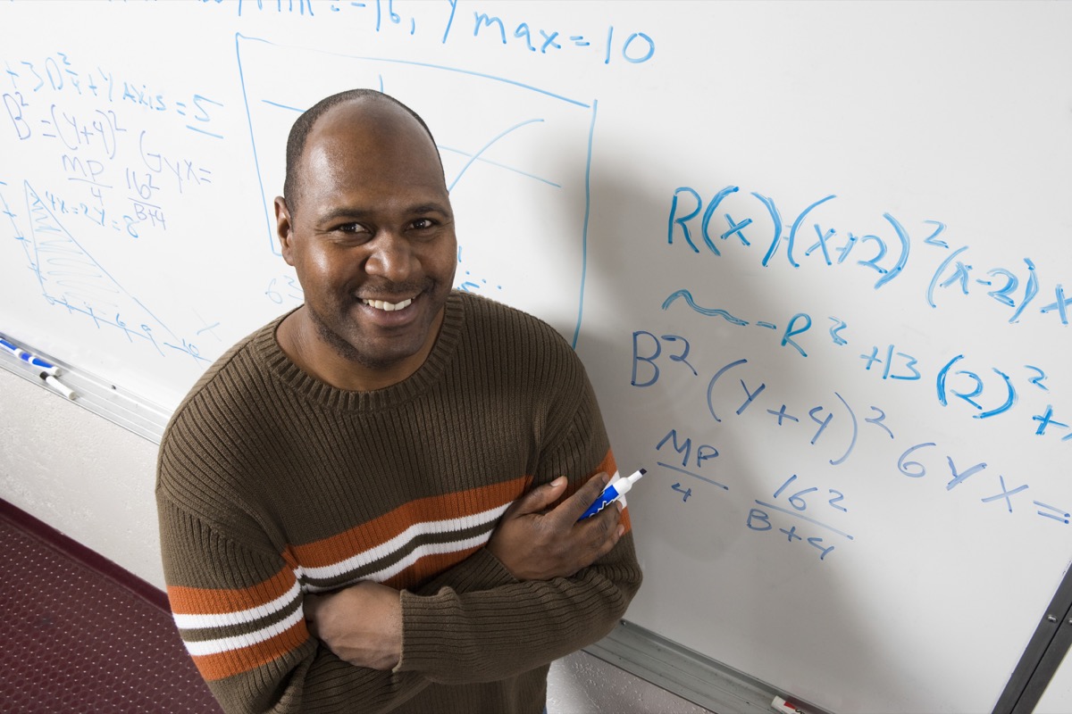 portrait of confident teacher solving math's equations on whiteboard in classroom