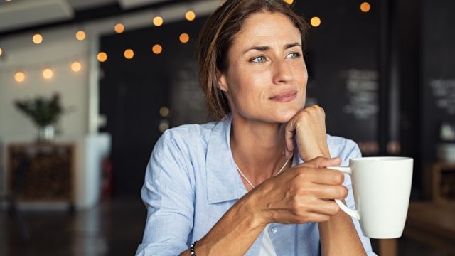 mature woman sitting in cafeteria holding coffee mug while looking away