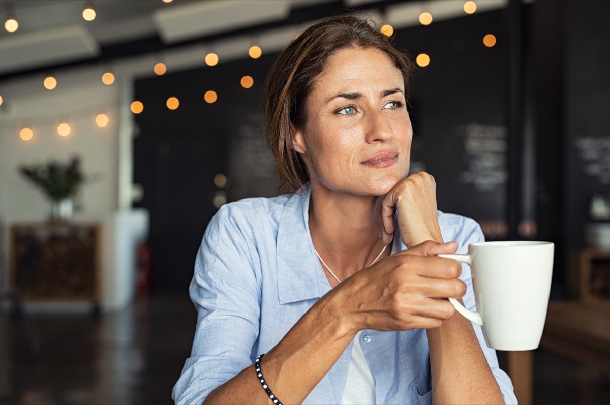 mature woman sitting in cafeteria holding coffee mug while looking away