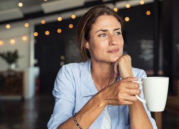 mature woman sitting in cafeteria holding coffee mug while looking away