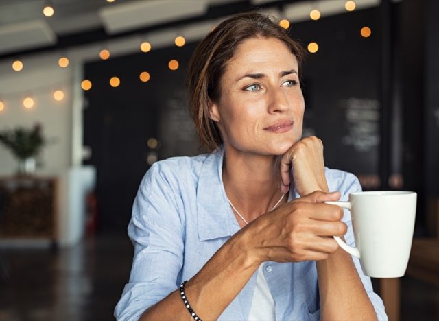 mature woman sitting in cafeteria holding coffee mug while looking away