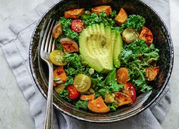 Bowl of paleo diet foods with kale, avocado, tomatoes, and potatoes