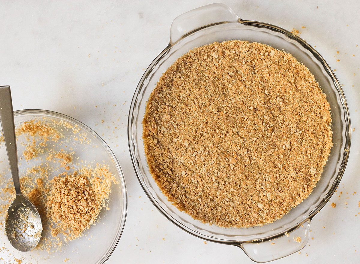 Graham cracker crust being pressed down into a pie pan