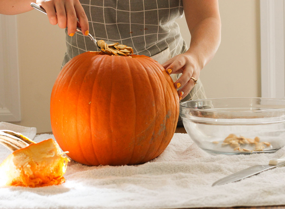 Scooping out pumpkin seeds into a bowl from a pumpkin