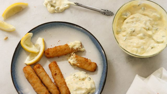 Tartar sauce with fish sticks and lemon wedges on a plate