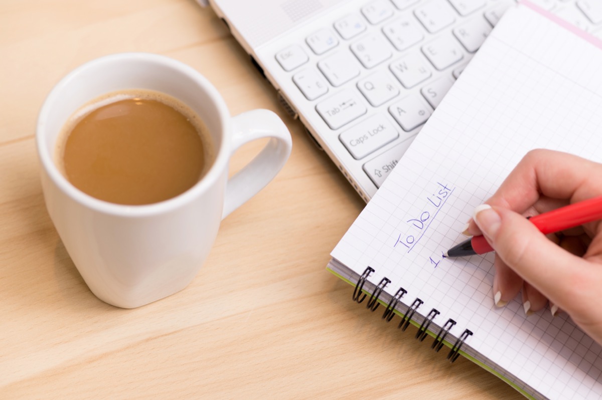 Woman writing a 'to do list' at her desk with a cup of fresh coffee
