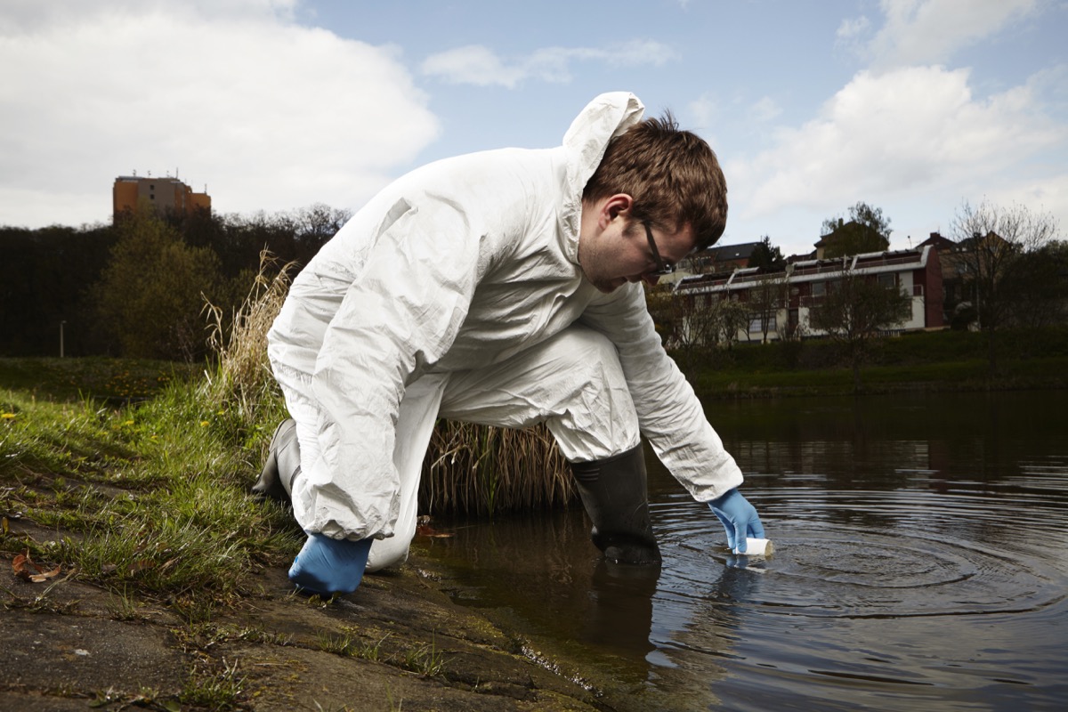 Man in overall protective suit collecting samples of water