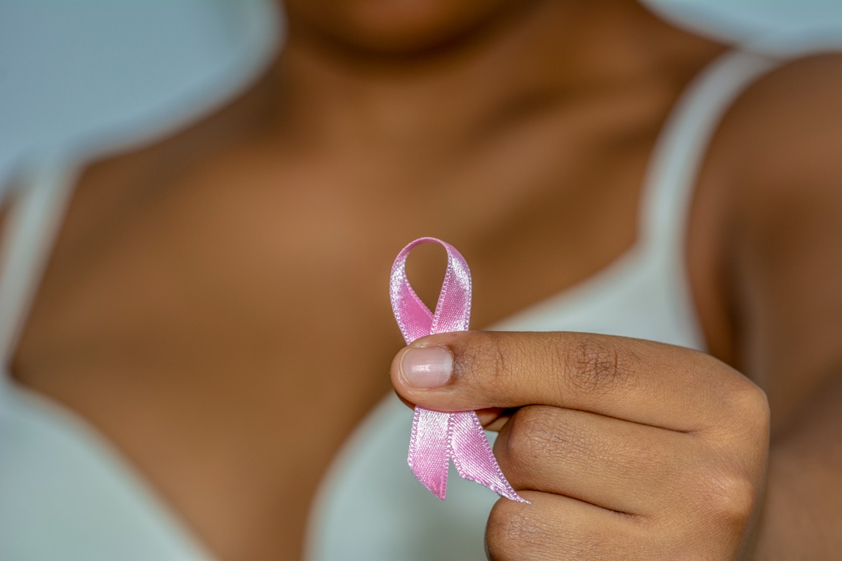 African woman's hand holding pink ribbon against breast cancer