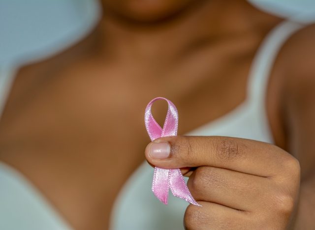 African woman's hand holding pink ribbon against breast cancer