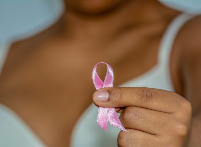 African woman's hand holding pink ribbon against breast cancer