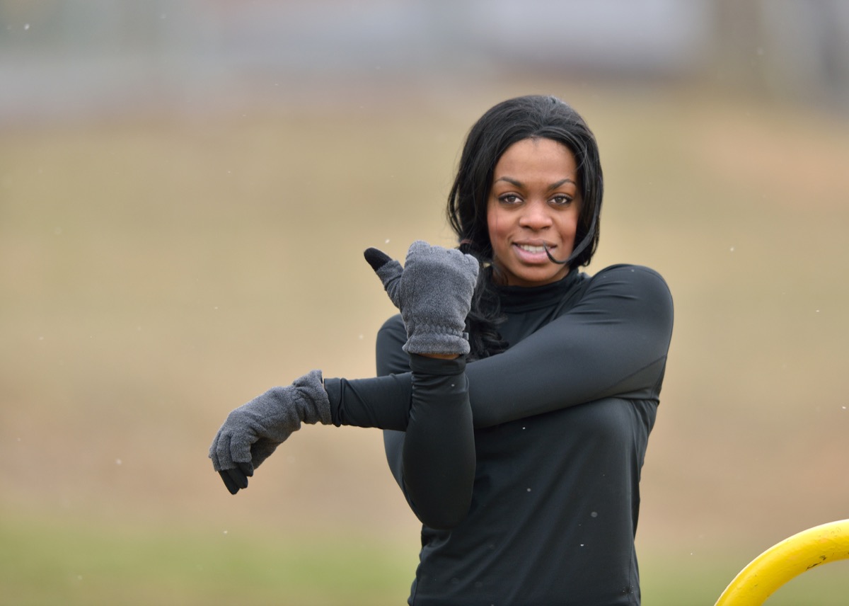 Woman in black fitness gear stretching in a park - cold weather