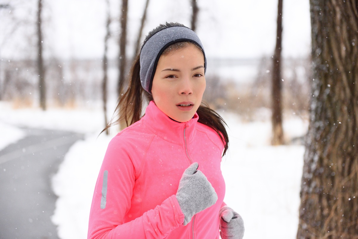 Woman running in cold weather wearing winter accessories, pink windbreaker, gloves and headband