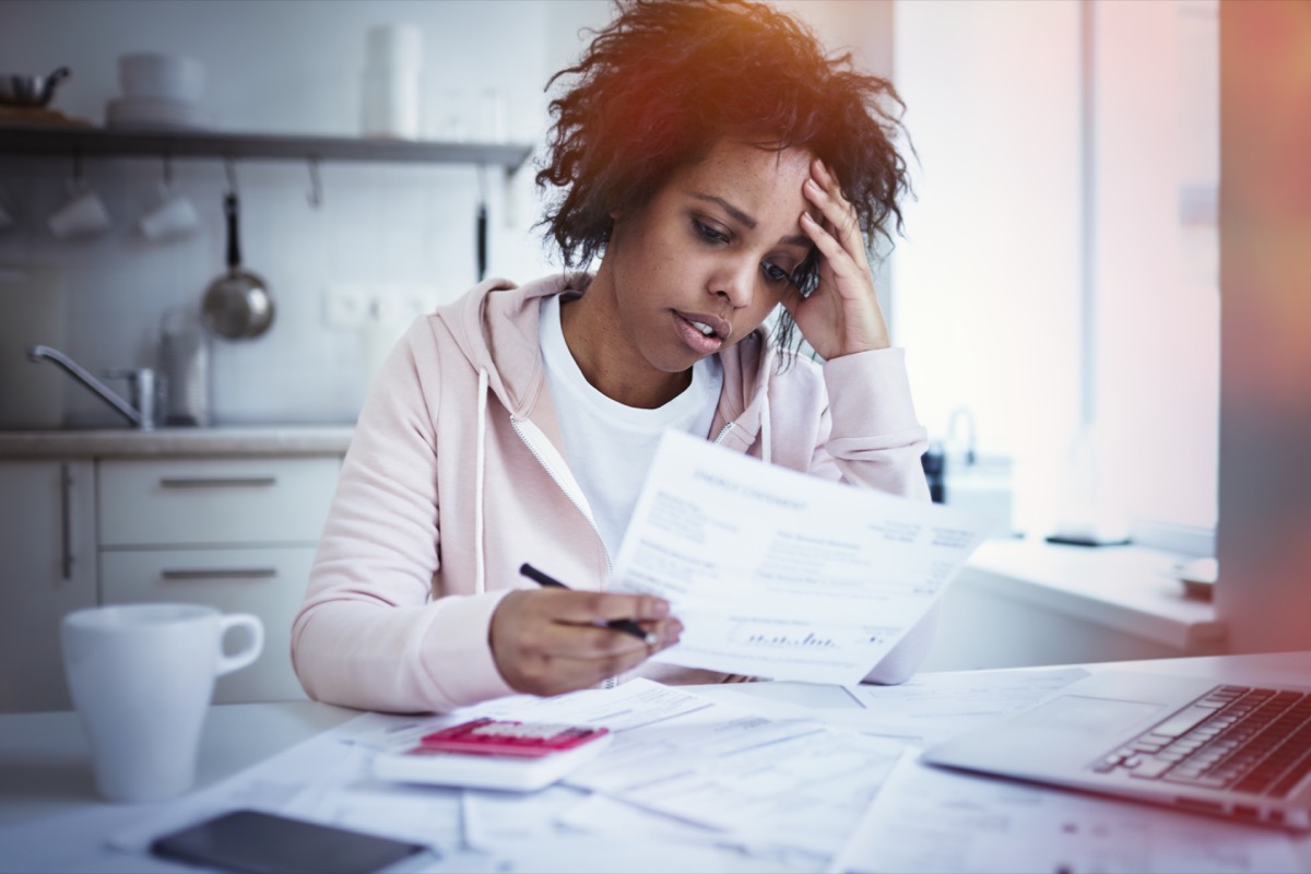 female sitting at kitchen table with laptop, dealing with financial stress