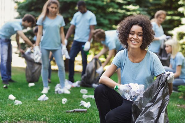 Happy woman and group of volunteers with trash bags cleaning area in the park, copy space