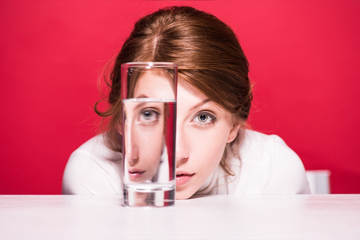 young woman looking through glass of water