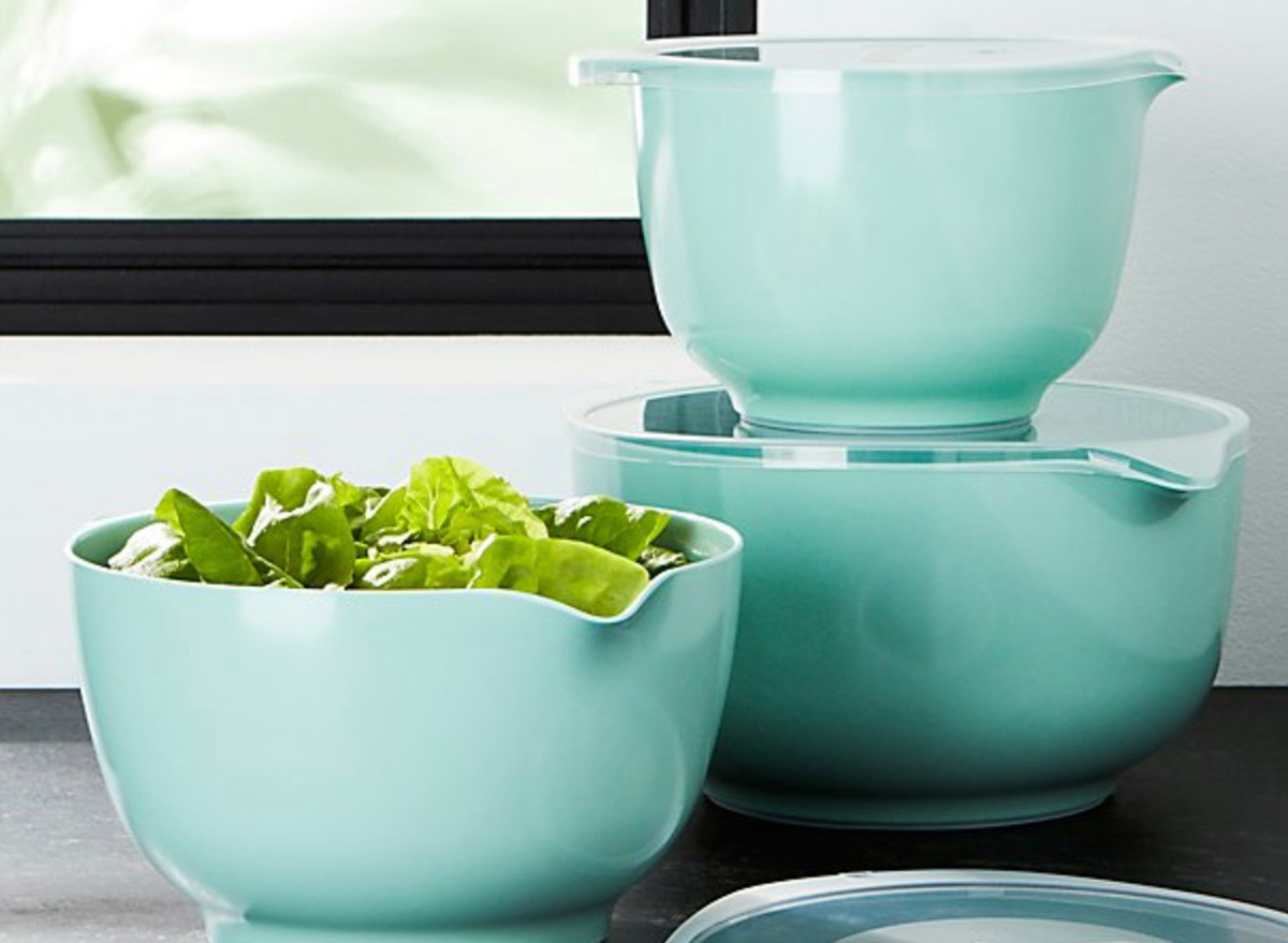 three turquoise mixing bowls, one with a salad in it, in front of black-framed window