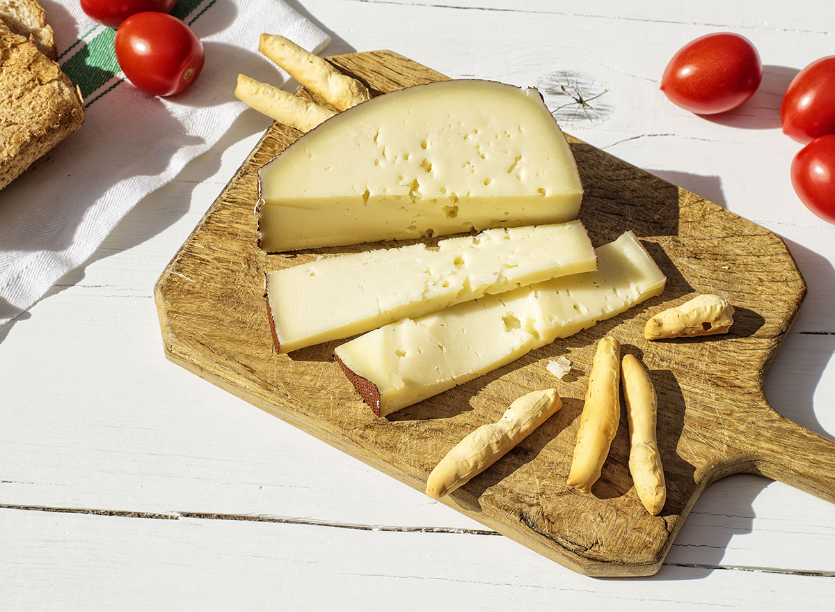 Asiago cheese sliced on a board with crackers and cherry tomatoes