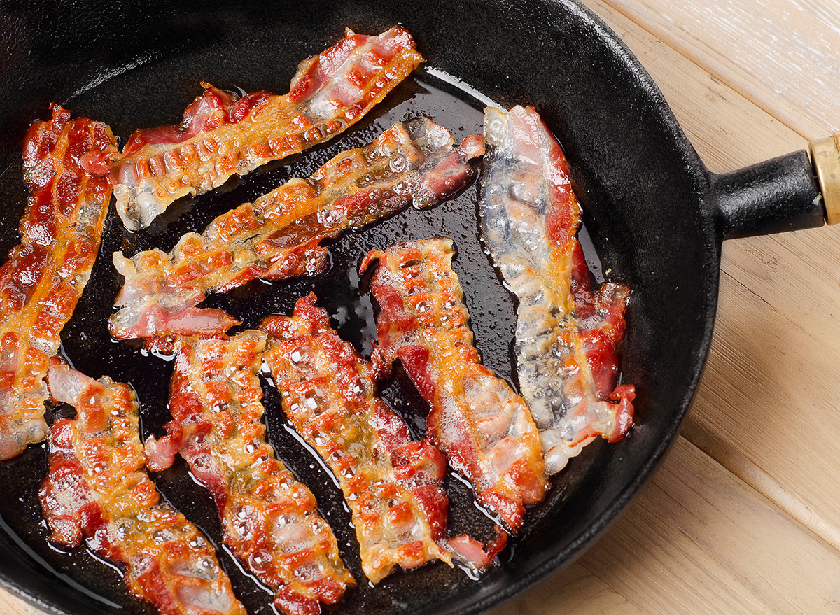 Bacon frying in stove top pan. Sizzling bacon strips in silver skillet.  Stock Photo