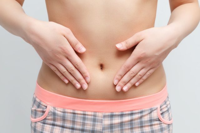woman's abdomen and belly button, she is touching her slim stomach with two hands