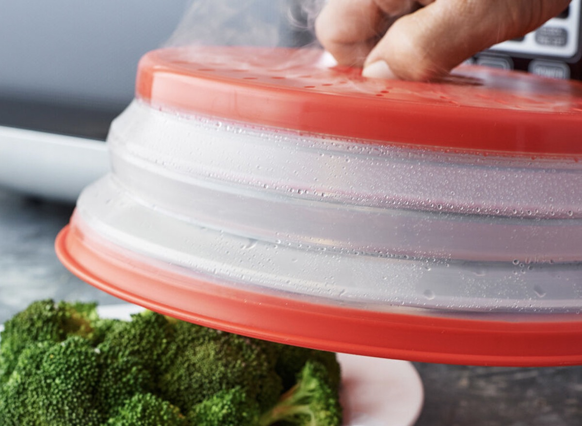 hand holding red and clear accordion cover over plate of broccoli