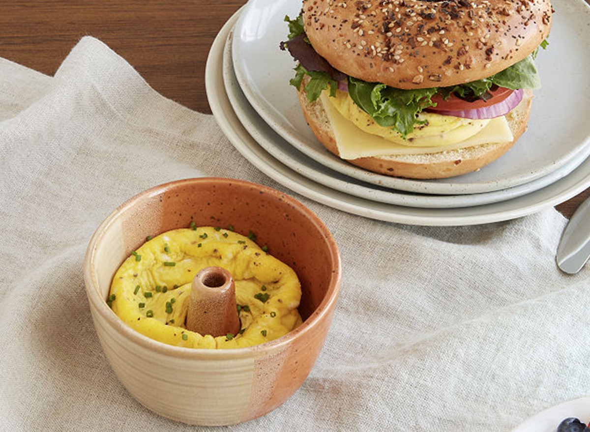 cup with eggs in it and stack of plates with bagel on it