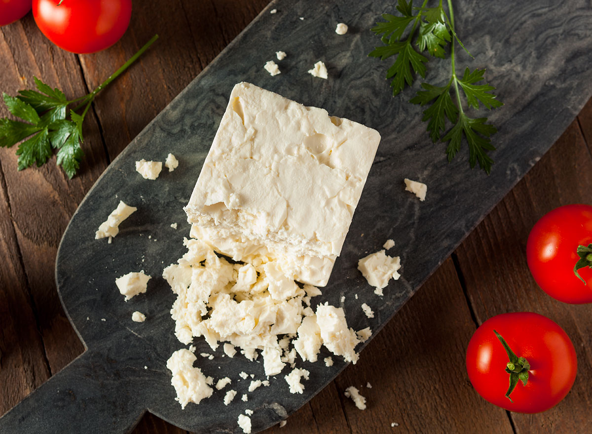 Broken up feta cheese on a board with tomatoes