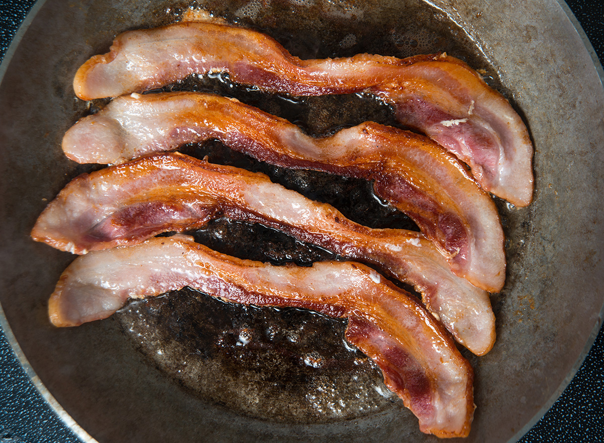 four pieces of bacon cooking in a pan