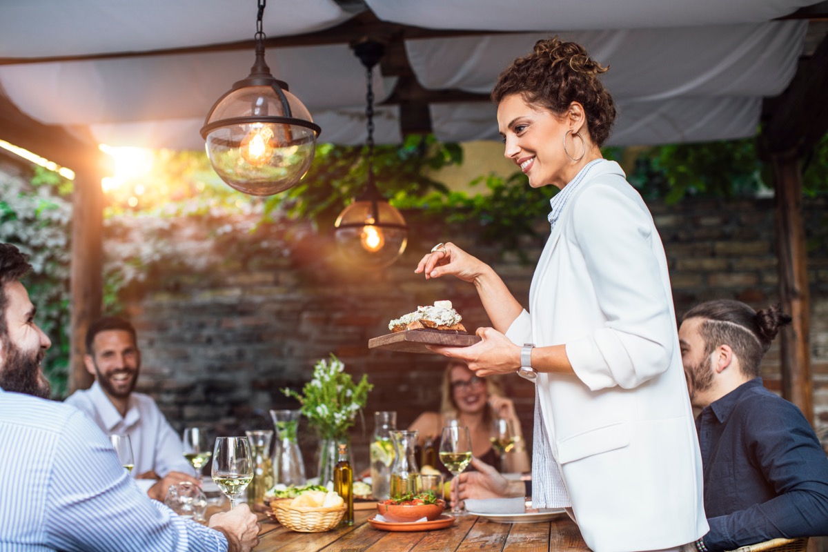 woman putting a plate with meal on dining table at backyard celebration