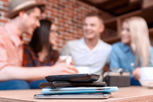 mobile phones lying on each other on the table and the company of young students having fun in a cafe while chatting