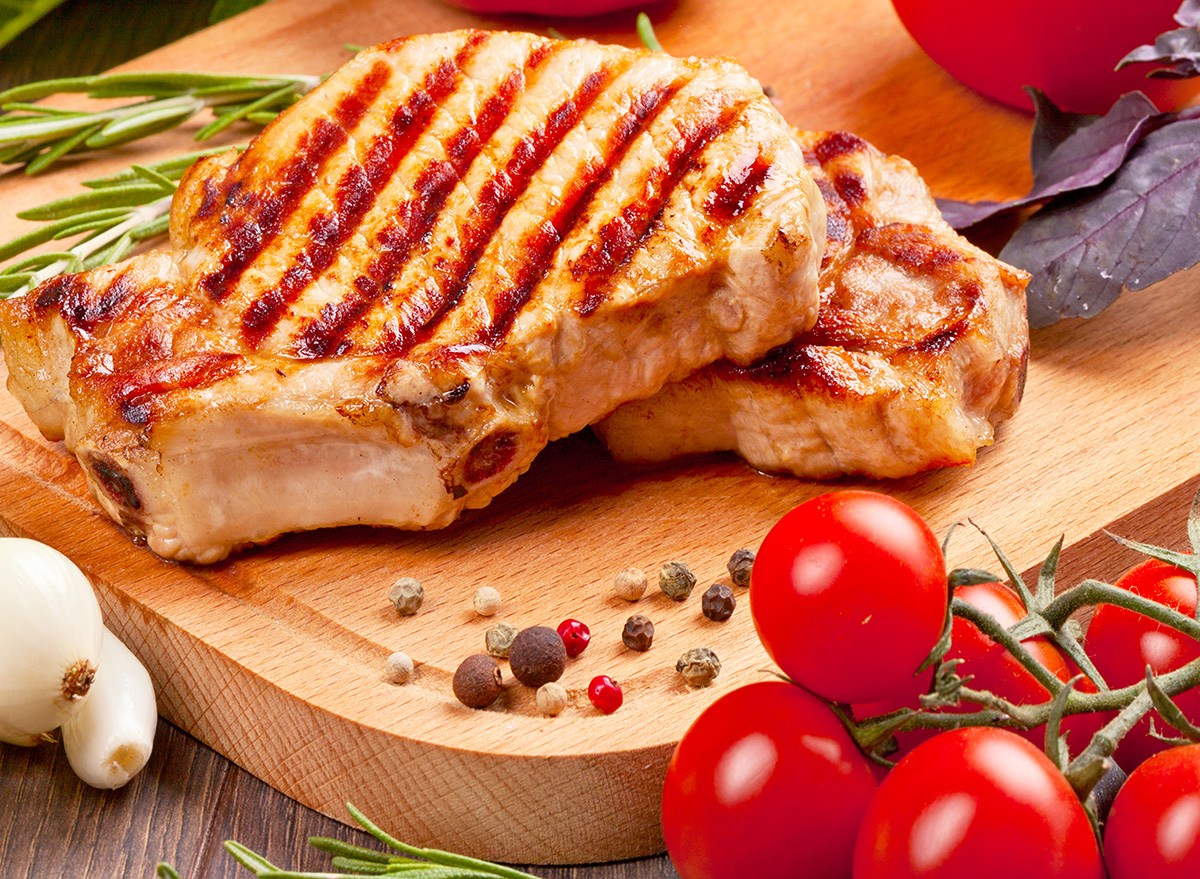 grilled pork chop on cutting board with tomatoes, garlic and peppercorn