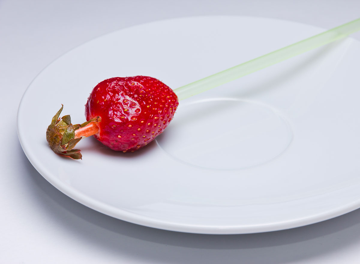 Hulled strawberry with a straw through it on a plate.