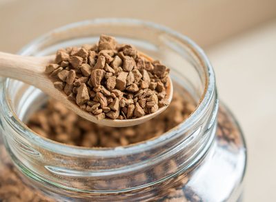 instant coffee crystals in spoon with glass jar