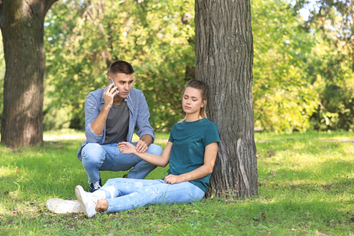 Passerby calling ambulance while checking pulse of unconscious woman outdoors