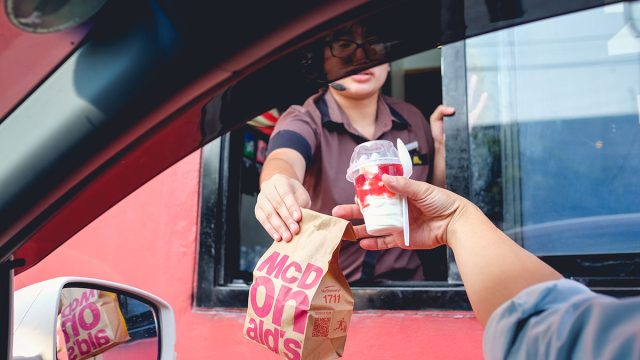 McDonald's employee handing customer food through the drive thru window