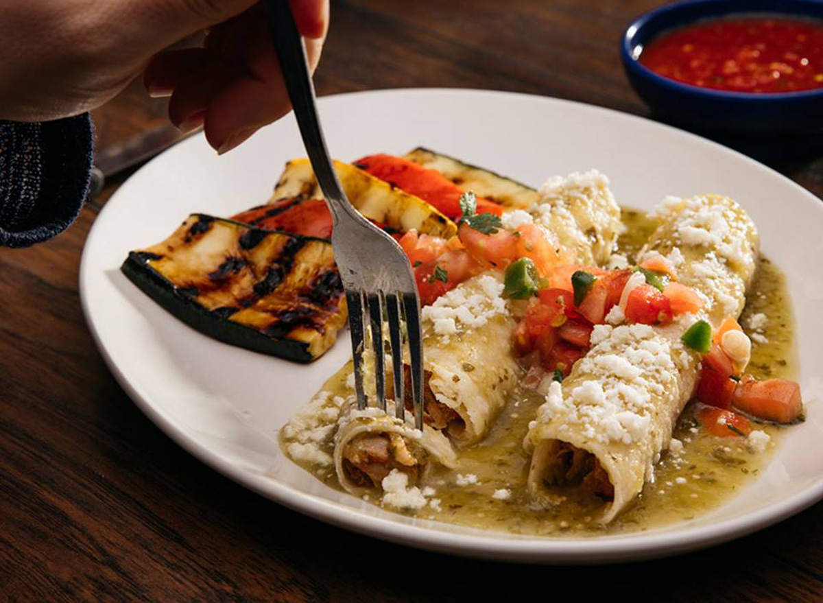 on the border tomatillo enchiladas on white plate with side of sautéed vegetables